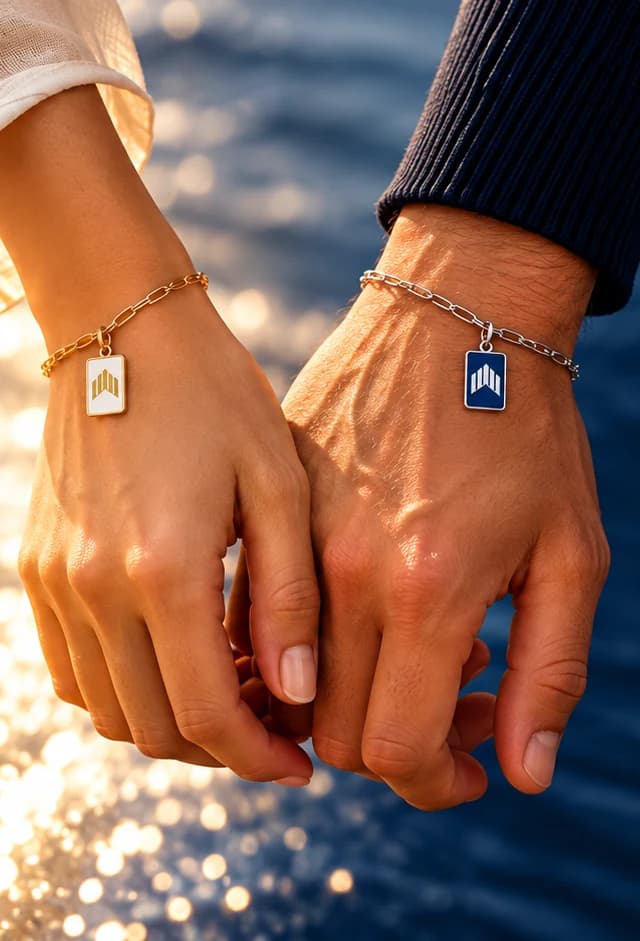 Two hands linked by Jewellery Club charm bracelets by the sea.